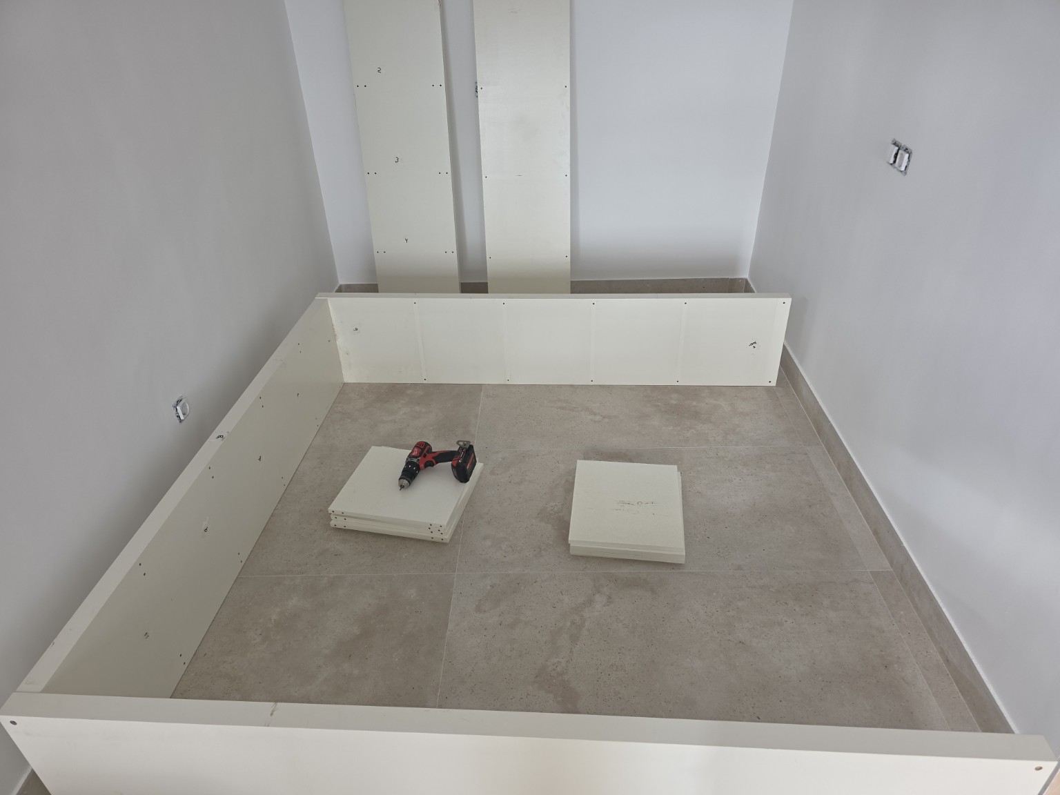 Paneles de un mueble desmontado, piezas agrupadas y un taladro en una habitación